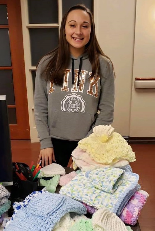 Girl with handmade baby blankets and hats 