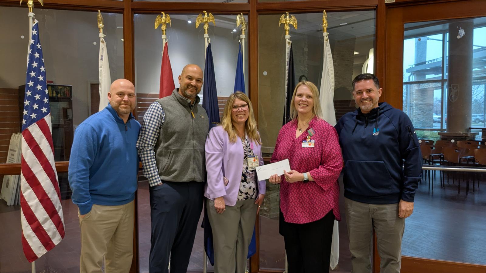 A group of five individuals pose for a photo while displaying a check for a donation.