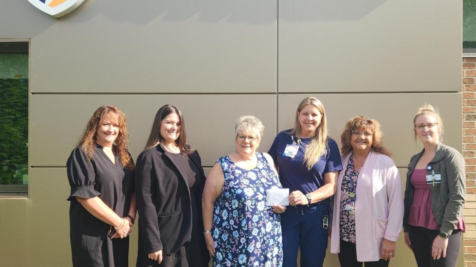 A group of women stand under a Guthrie sign while holding a check.