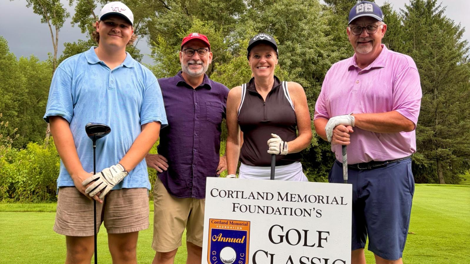 Four people stand on a golf course. 
