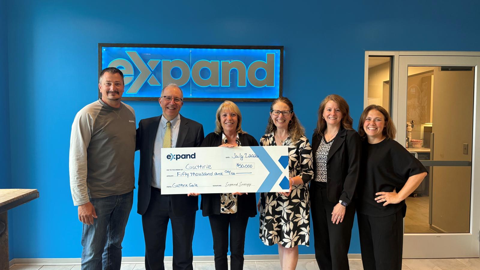 A group of people pose while holding a large check.