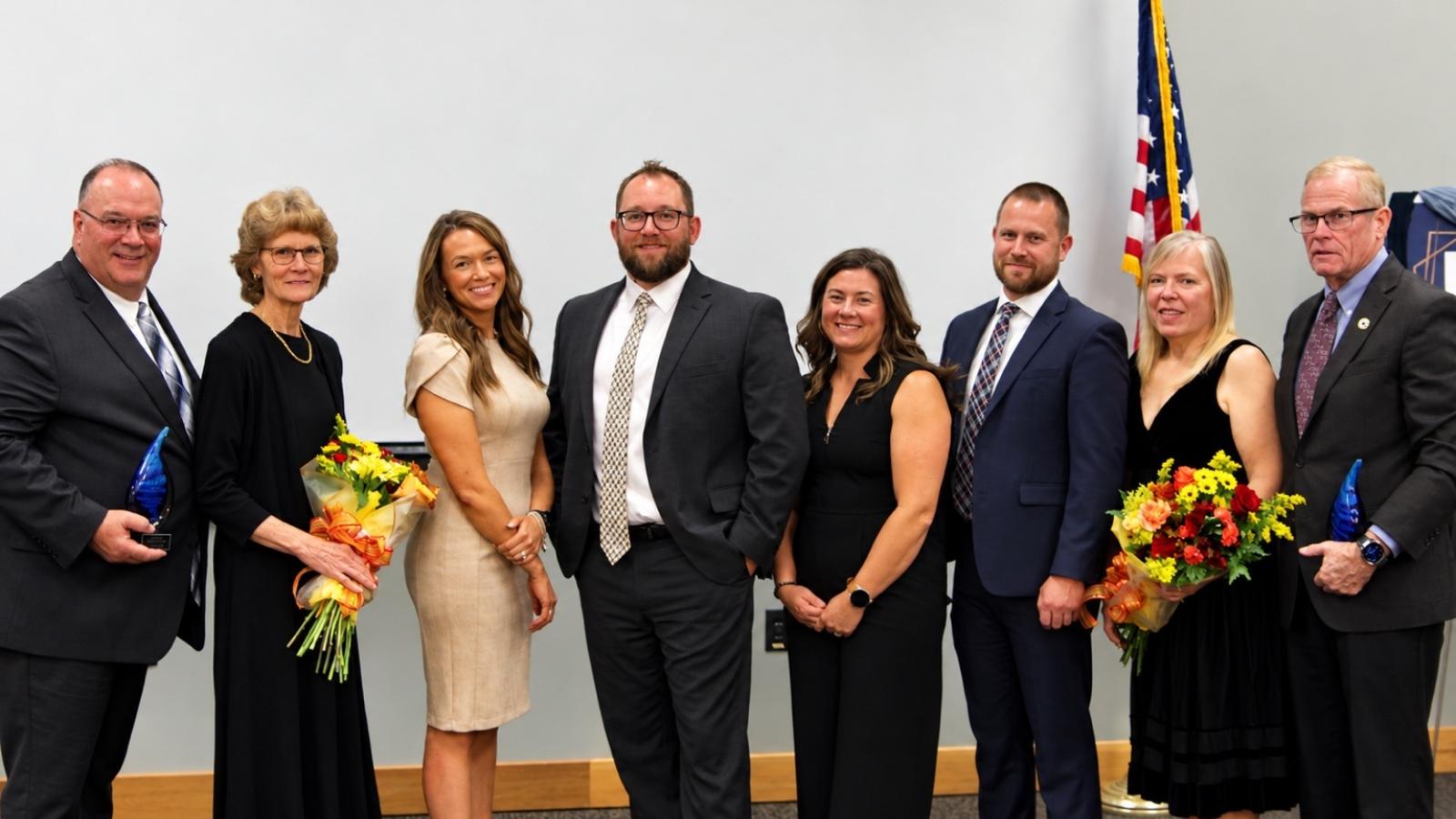 A group of eight people in dress attire pose for a photo.