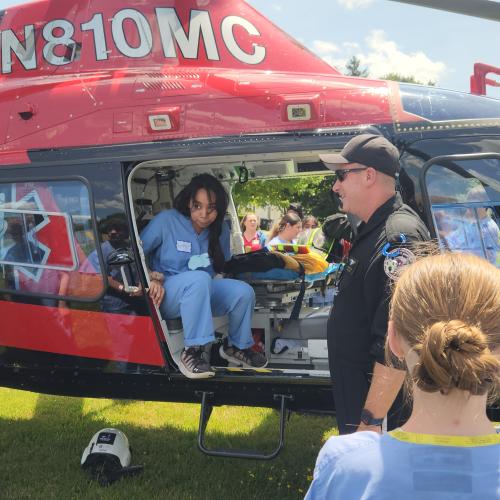 Students in medical scrubs gather around a helicopter and talk with one of the crew. One of the students is sitting in the helicopter.