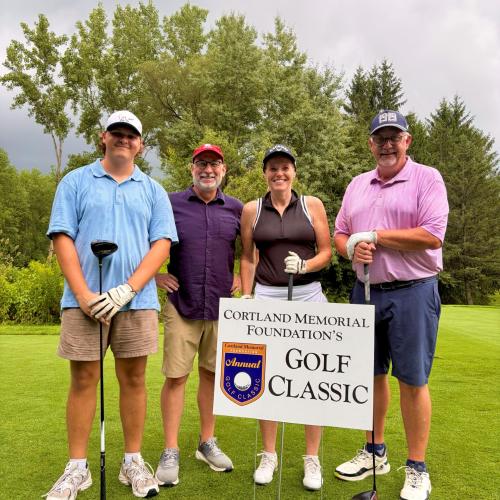Four people stand on a golf course. 