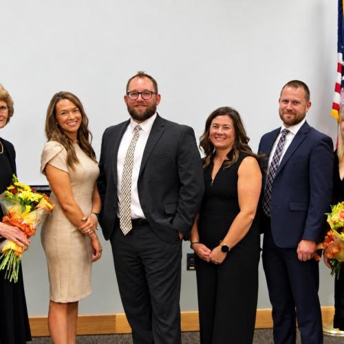 A group of eight people in dress attire pose for a photo.